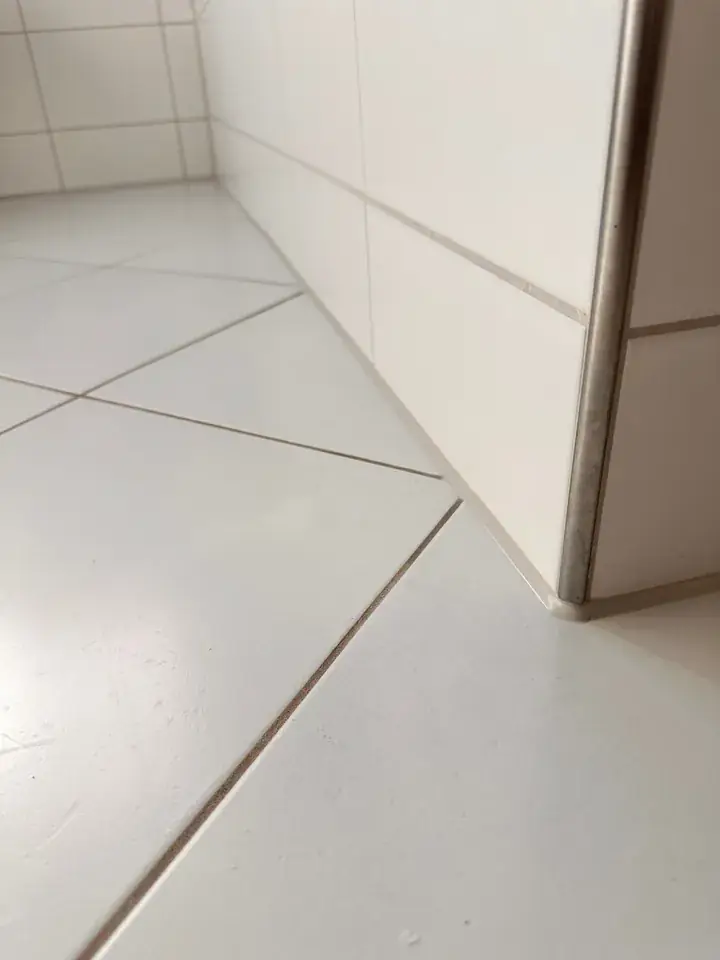 Dieselbe Wandecke mit sauberem Boden und einer schmalen, hellen Fuge an der Wand und bis zur Ecke