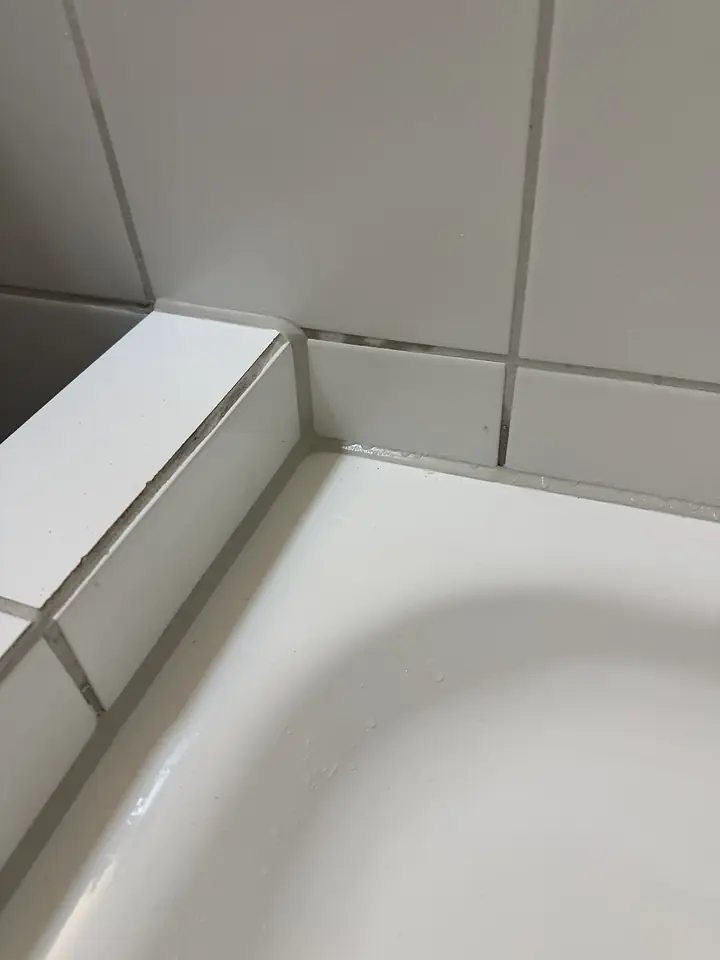 Dieselbe Badewannenecke am Mauervorsprung mit schmaler grauer Fuge zwischen Wanne und Wandplatten, ohne schwarze Punkte