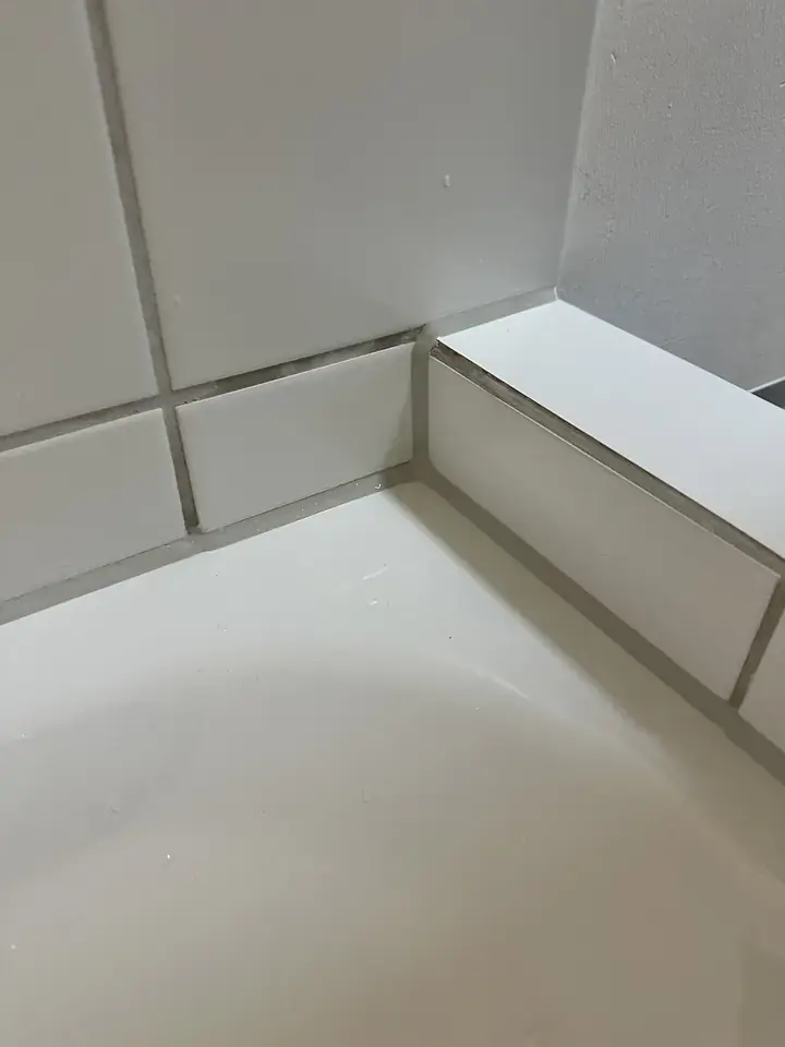 Ecke zwischen Badewanne und gefliestem Vorsprung mit grauen Fugen am Wannenrand und an den Plattenkanten