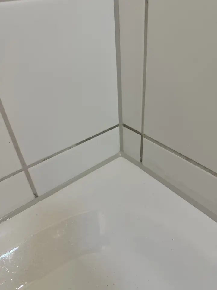 Dieselbe Wandecke über der Badewanne mit gleichmässigen grauen Fugen in der Ecke und am Wannenrand