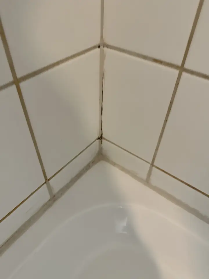 Dunkle alte Silikonfuge in der Wandecke über einer Badewanne