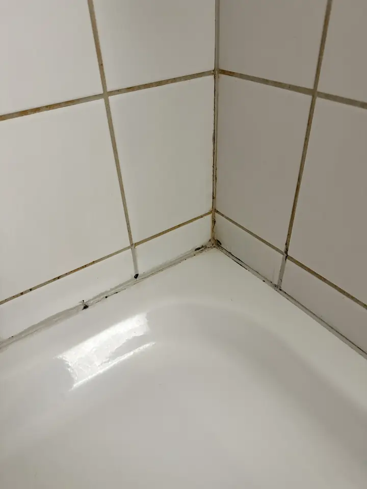 Dunkel verfärbte alte Silikonfuge mit schwarzen Punkten in der Ecke einer Badewanne