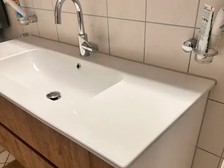 Weisser Waschtisch mit Einhebelmischer auf Holzunterschrank vor hellen Wandplatten, rechts an der Wand ein Glashalter