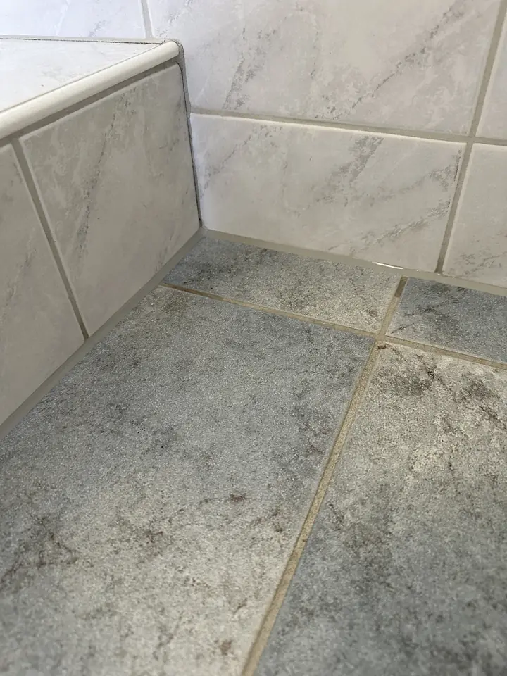 Dieselbe Ecke mit durchgehender grauer Fuge zwischen Boden, Wand und gefliester Wannenverkleidung