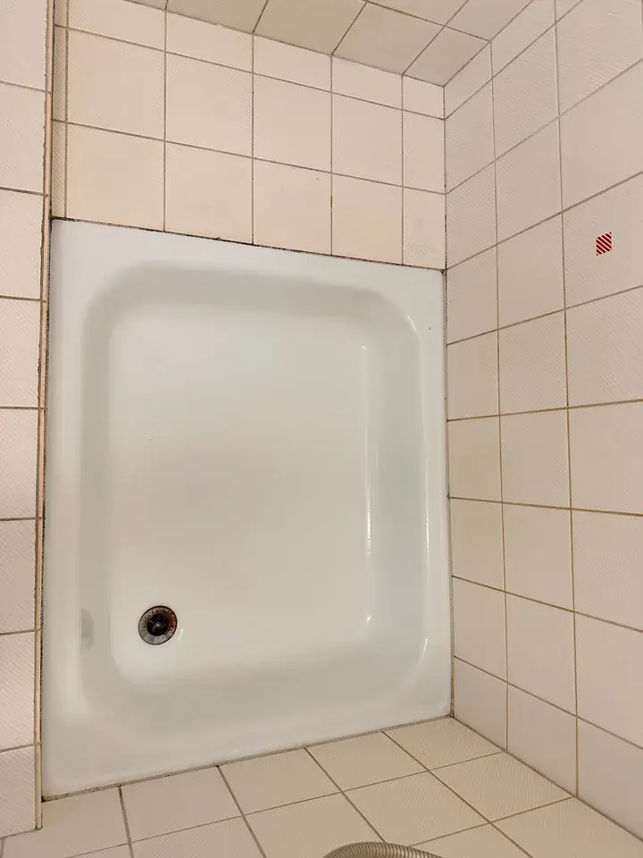 Weisse Duschtasse in einer Wandnische mit cremefarbenen Platten, am Tassenrand verläuft eine dunkle Linie