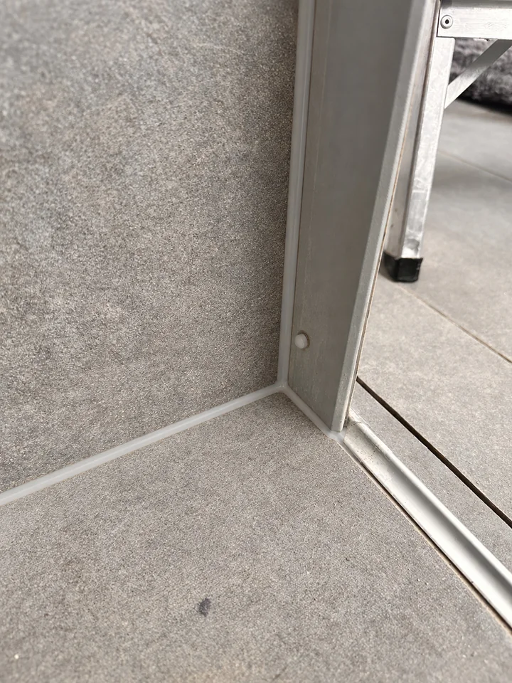 Dieselbe Ecke aus grauen Platten und Metallprofil, am Boden und am Profil verläuft eine helle Fuge