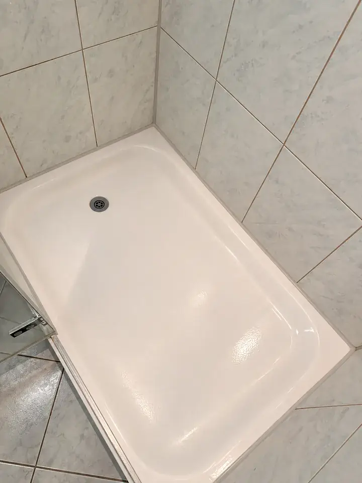 Weisse Duschtasse mit heller Fuge am Rand vor hellen, marmorierten Wandplatten