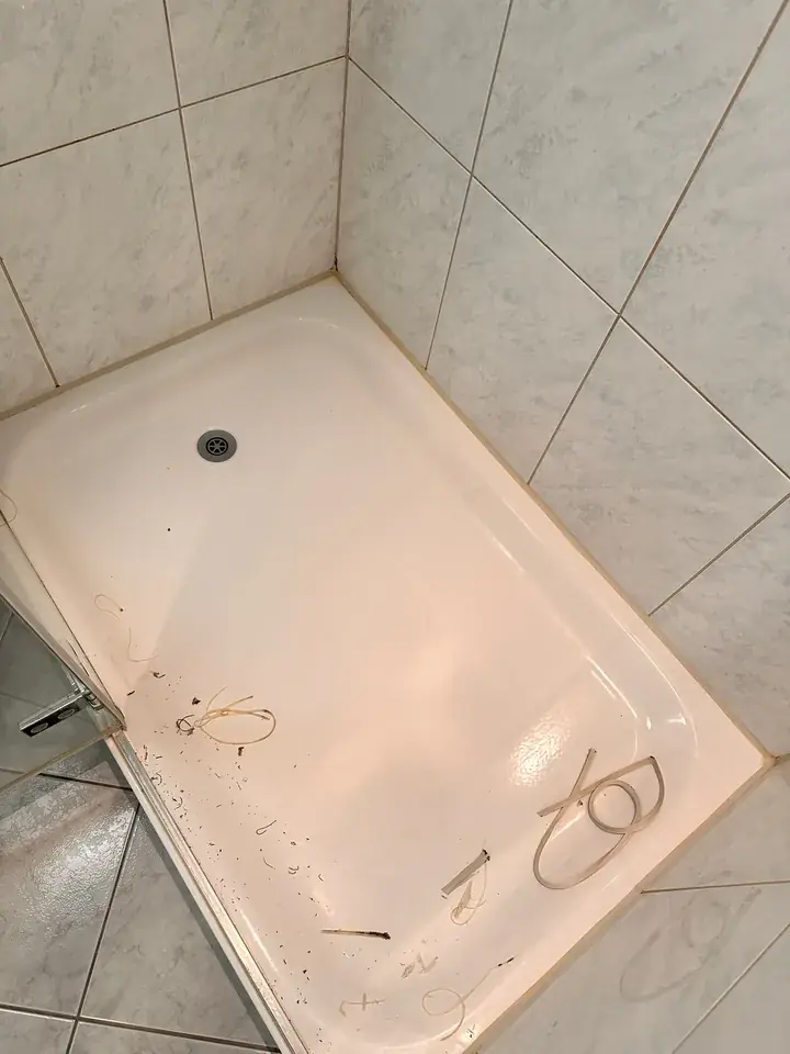 Alte verfärbte Silikonfuge am Rand einer weissen Duschtasse vor marmorierten Wandplatten
