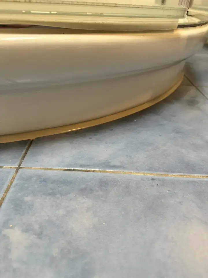 Runde weisse Duschwanne auf blauen Bodenplatten, am Fuss der Wanne verläuft ein beiges Band zum Boden