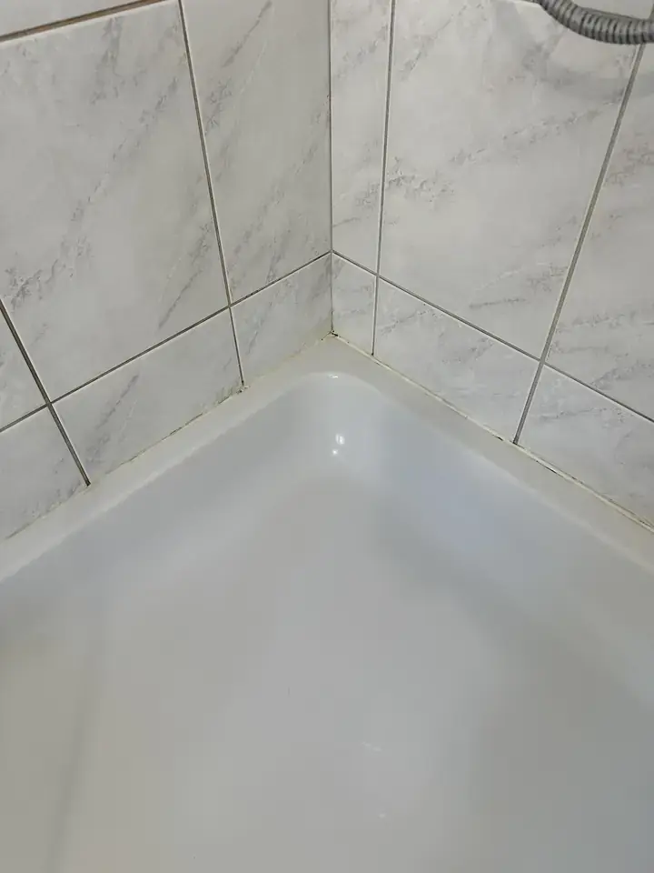 Weisse Duschwanne in der Ecke vor weissgrauen Platten in Marmoroptik, am Rand der Wanne einzelne dunkle Punkte