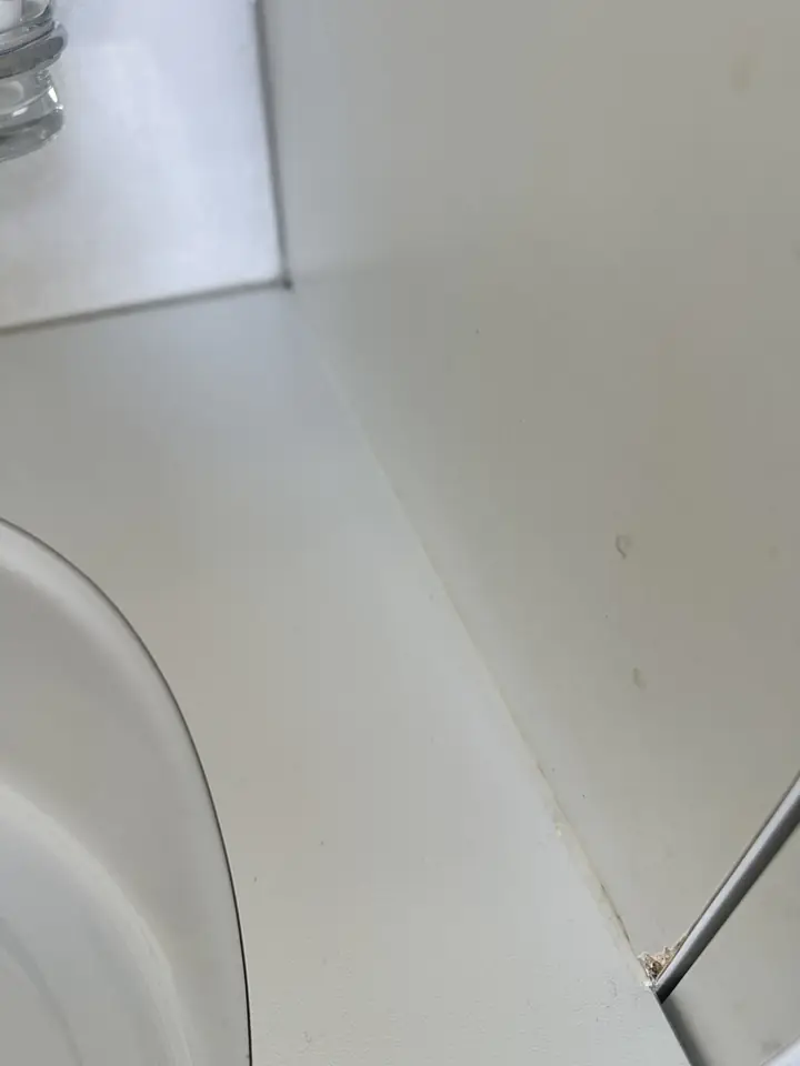 Weisse Ablage einer Eckbadewanne an der Wand, unten rechts an der Kante eine kleine braune Stelle