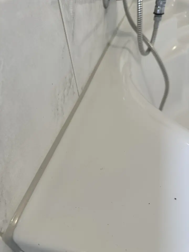 Dieselbe Eckbadewanne, am Wannenrand zur marmorierten Wand verläuft eine schmale graue Fuge, daneben der Brauseschlauch