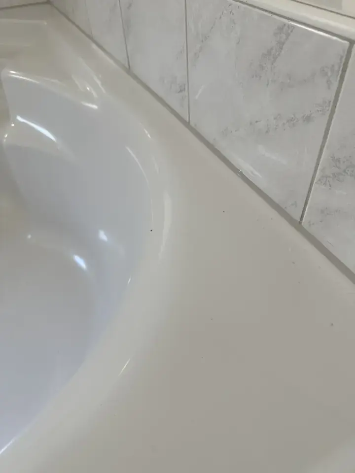 Derselbe Wannenrand vor den Marmoroptik-Platten, zwischen Wanne und Platten verläuft eine graue Linie