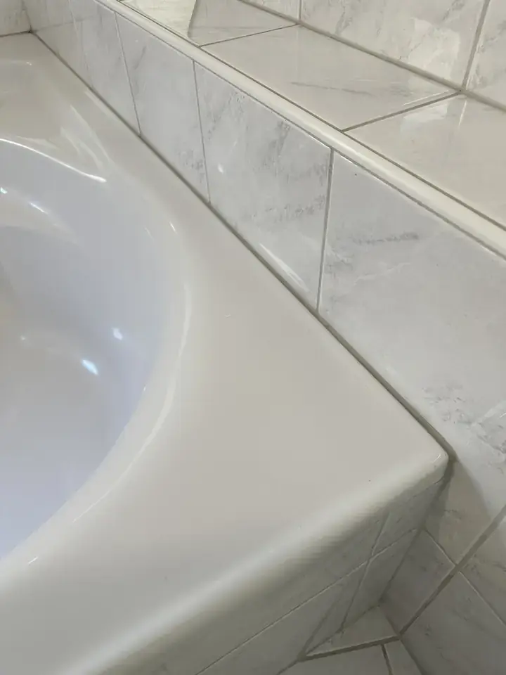 Eckbadewanne vor weissen Platten in Marmoroptik, zwischen Wannenrand und Platten verläuft eine schmale dunkle Linie