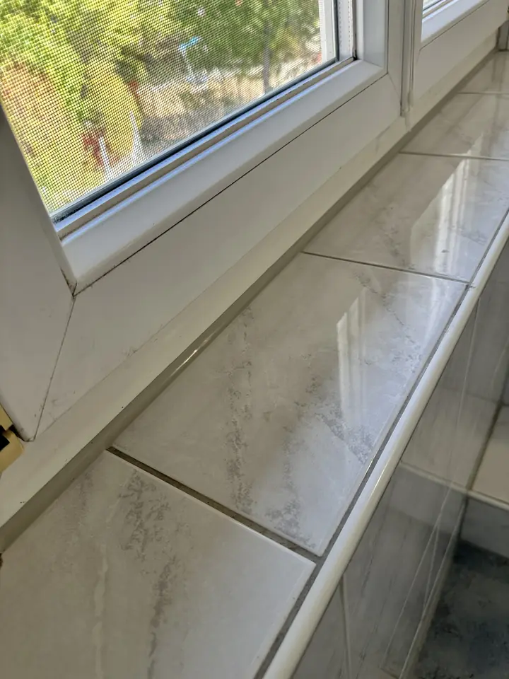 Geflieste Fensterbank unter einem Fenster mit weissem Rahmen, am vorderen Rand eine weisse, abgerundete Kante