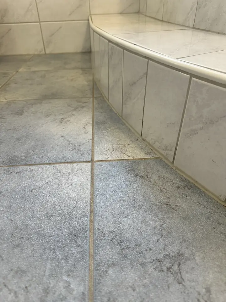 Gebogene Wannenverkleidung aus hellen Platten auf grauem Fliesenboden, die Fuge am Boden wirkt gelblich