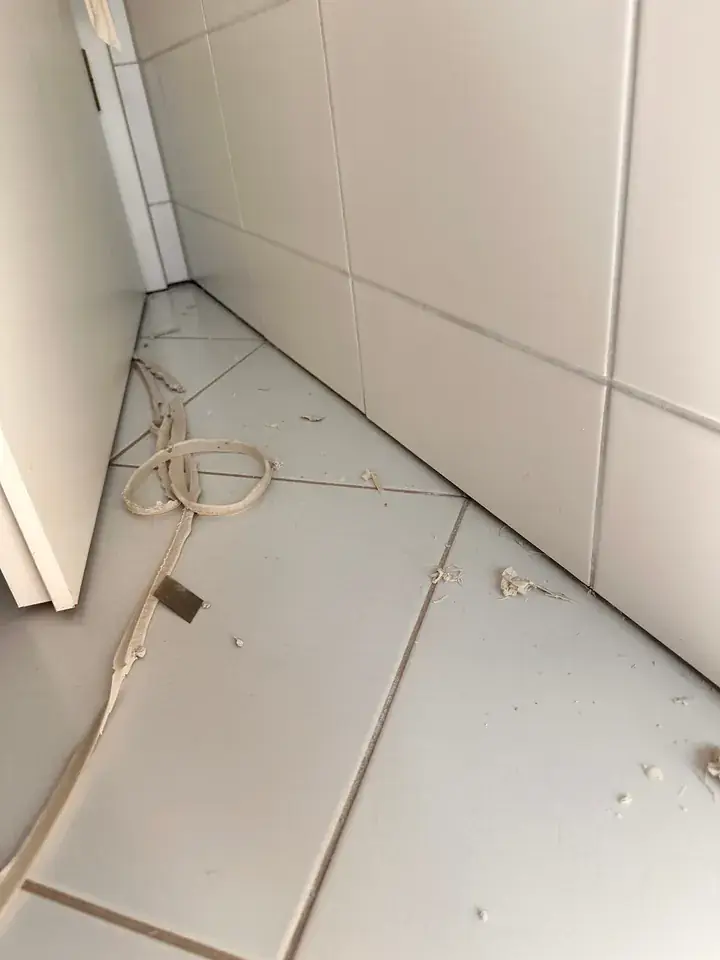 Helle Wand- und Bodenplatten neben einer Tür, auf dem Boden liegen ein langer Silikonstreifen und Silikonkrümel