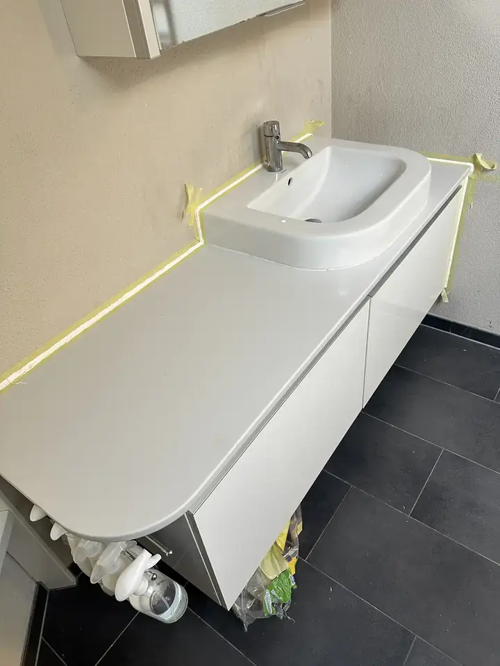 Weisser Waschtisch an beiger Wand, entlang der Wand und an der Seite klebt gelbes Malerband