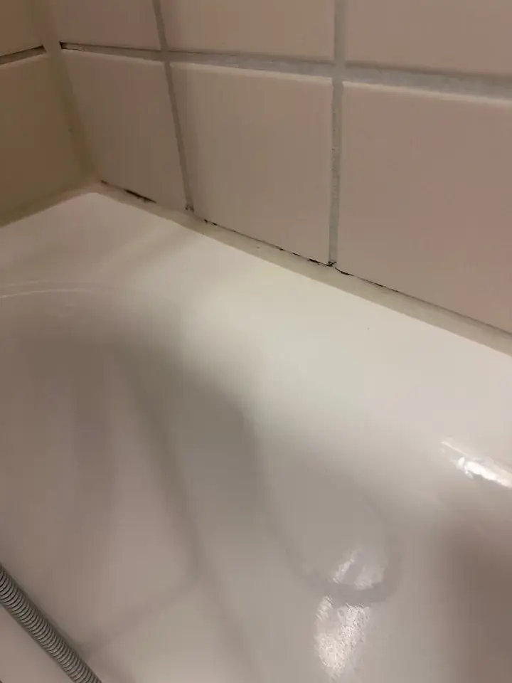 Weisse Badewanne an kleinen rosabeigen Wandplatten, in der Kante zwischen Wanne und Platten zeichnen sich dunkle Stellen ab