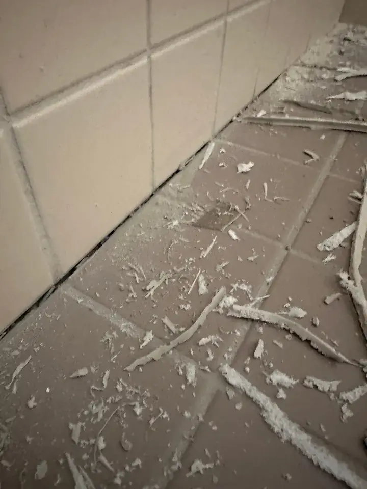Schmaler offener Spalt zwischen beigen Wandplatten und braungrauen Bodenplatten, auf dem Boden liegen Reste von Silikon