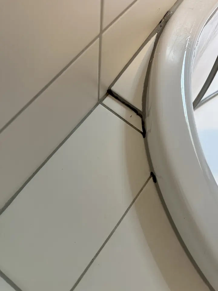 Runder weisser Wannenrand vor weissen Wandplatten, an einer Plattenecke verläuft eine dunkle Linie in Winkelform