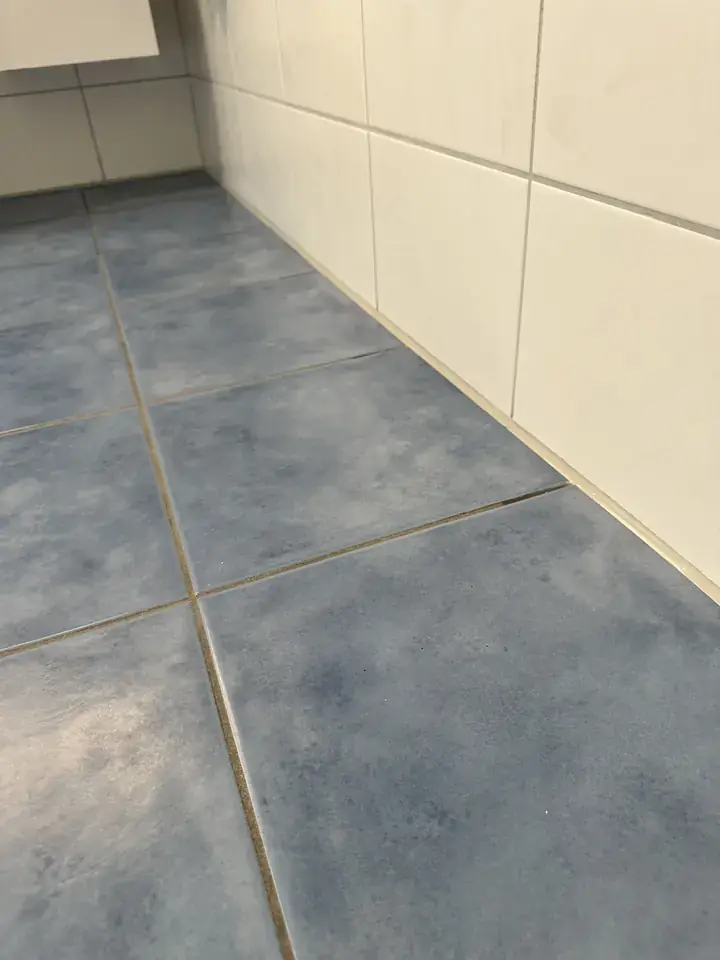 Dieselben blauen Bodenplatten und hellen Wandplatten, entlang der Kante zur Wand verläuft eine helle Fuge