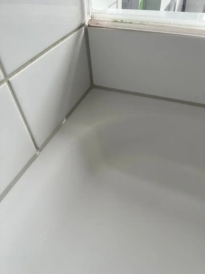 Wannenrand und Wandecke mit grauer Fuge, oben ein Fenster mit Rahmen