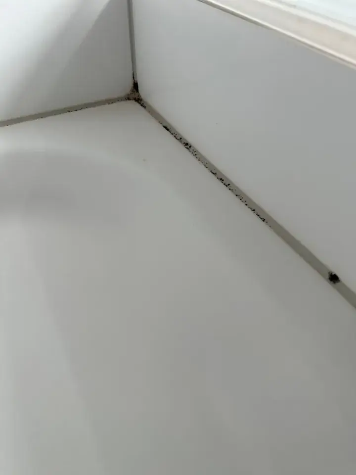 Weisser Wannenrand mit Wandplatten, dunkle Flecken in der Fuge entlang der Kante und in der Ecke