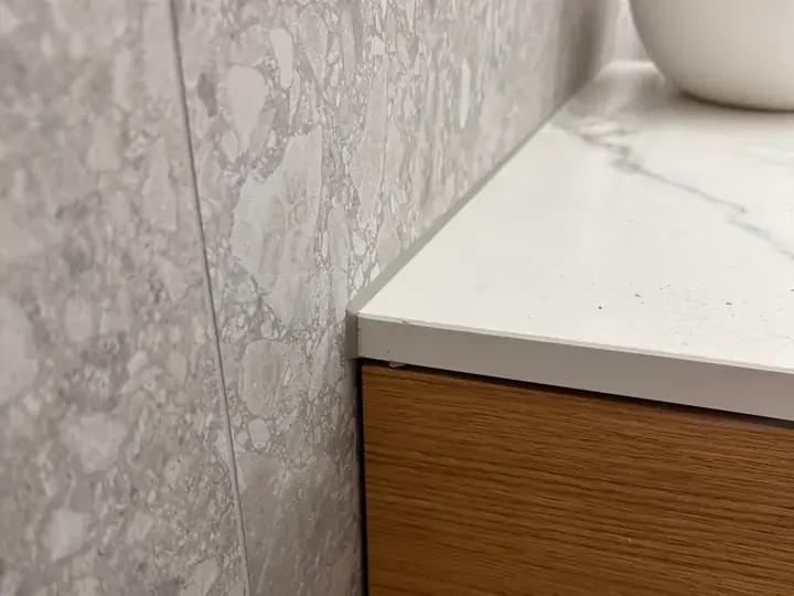 Helle Waschtischplatte in Marmoroptik an einer grau gemusterten Wand über einem Unterschrank aus Holz