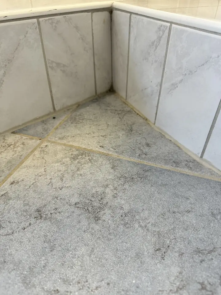 Ecke an einer gefliesten Wannenverkleidung mit grauem Boden in Steinoptik, gelbliche Linien an Kante und Bodenfugen