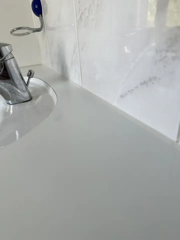 Weisse Ablage am Waschbecken mit Armatur vor Wandplatten in Marmoroptik, entlang der Kante eine schmale helle Fuge