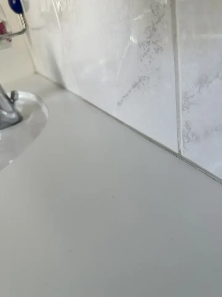 Weisse Ablage am Waschbecken vor Wandplatten in Marmoroptik, entlang der Kante verläuft eine dünne dunkle Fuge
