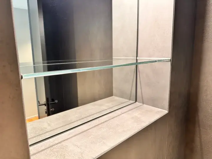 Wandnische mit Glasablage und Spiegel, innen mit grauen Platten verkleidet, im Spiegel spiegelt sich der Raum