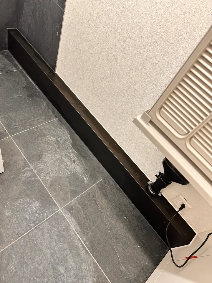Dunkelgrauer Plattenboden mit schwarzer Sockelleiste an einer weissen Wand, rechts am Bildrand ein Heizkörper