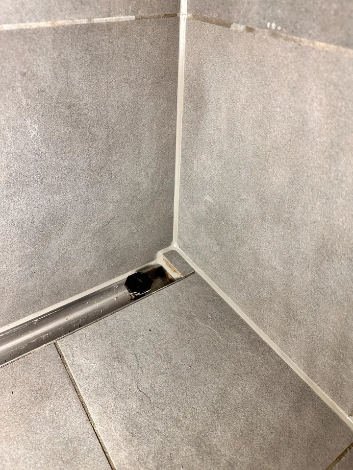 Dieselbe Duschecke mit grauen Wandplatten und Ablaufrinne, in der Ecke und am Boden verläuft eine helle Fuge