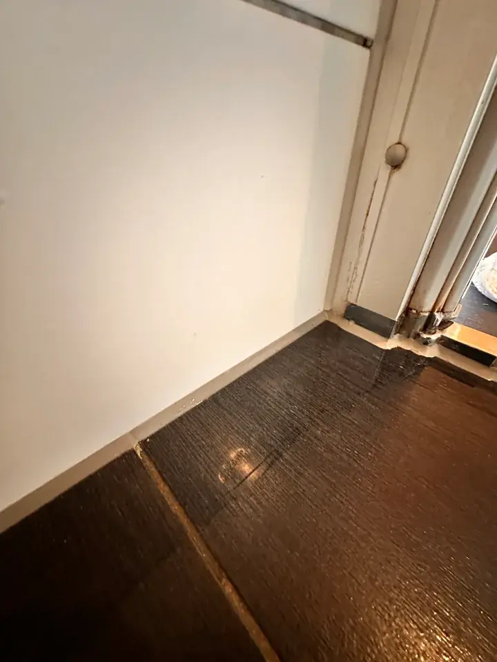 Dunkler Plattenboden mit hellem Streifen am Fuss der weissen Wand, rechts im Bild ein Türrahmen