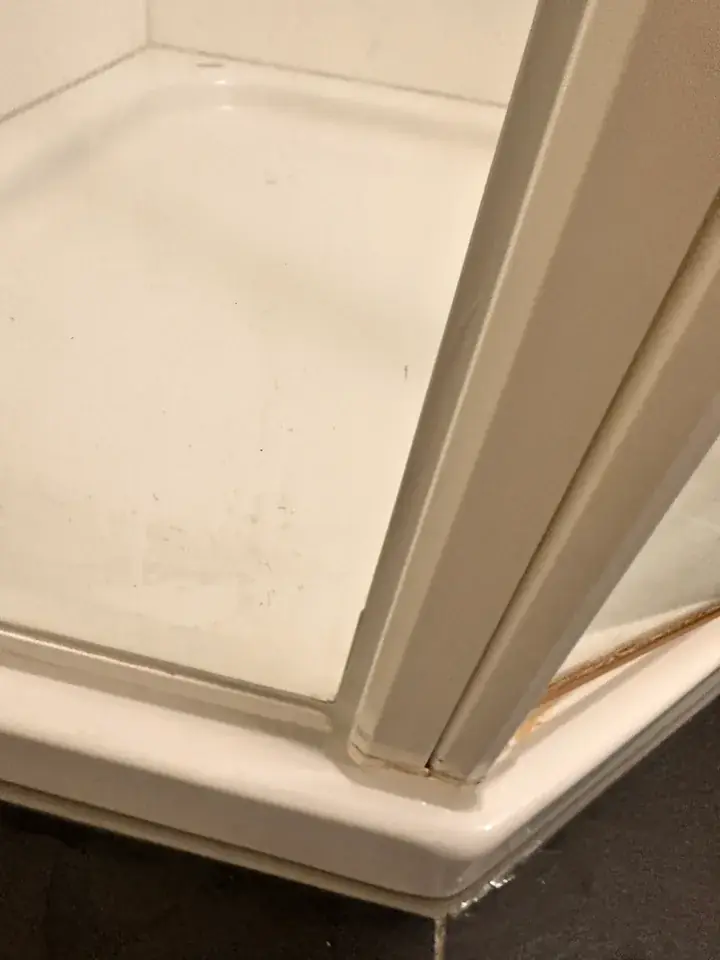 Weisse Duschtasse mit senkrechtem weissem Profil und Glas der Duschwand rechts, dunkler Boden im Hintergrund