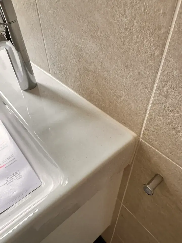 Dasselbe Lavabo vor beigen Reliefplatten, am Übergang zur Wand ein heller Streifen ohne dunkle Punkte