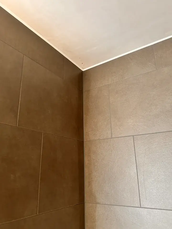 Obere Ecke zweier Wände mit braunen und beigen Platten unter heller Decke, am Übergang verläuft eine schmale helle Linie