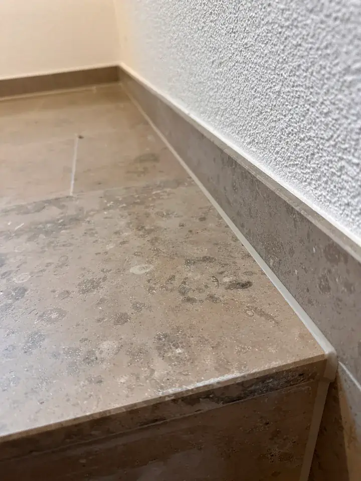Graue Steinstufe mit Sockel an einer weiss verputzten Wand, entlang der Sockelkante verläuft eine helle Fuge