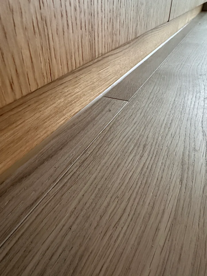 Eichenparkett an einer Holzverkleidung mit Sockelleiste, am Übergang verläuft ein schmaler heller Streifen